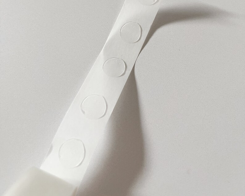 Detail of transparent glue dots roll unrolled. Each dot is double-sided and .47" round. 100 glue stickers per roll.