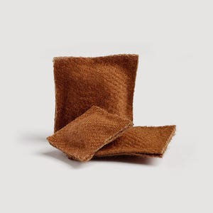 May include: Three brown, textured, square-shaped items are arranged on a white background. One is upright, and two are lying down. The items appear to be made of a soft, woven material.