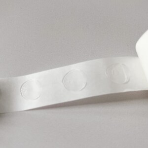 Detail of transparent glue dots roll unrolled. Each dot is double-sided and .47" round. 100 glue stickers per roll.