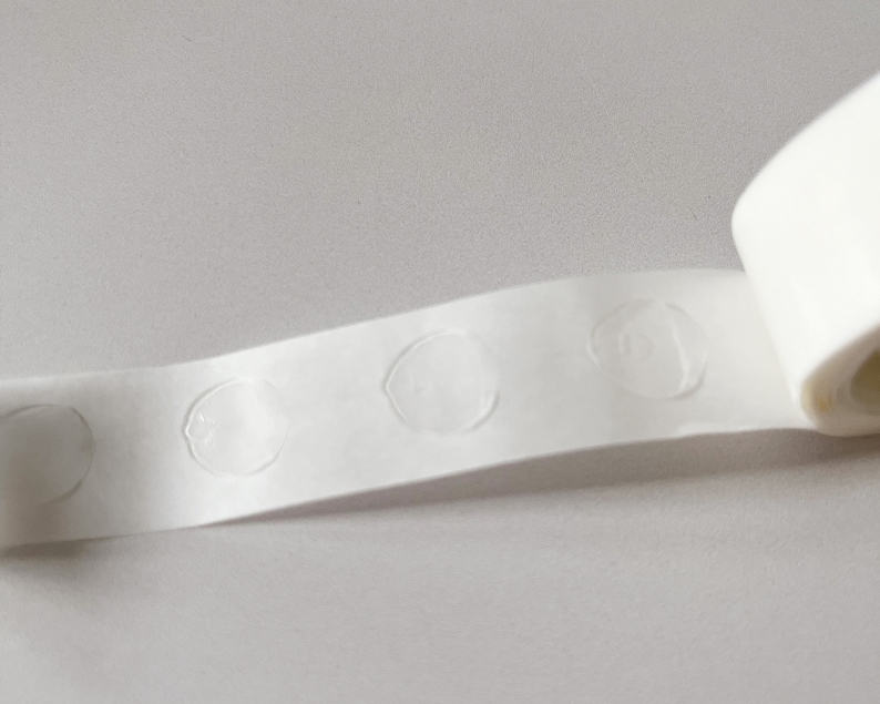 Detail of transparent glue dots roll unrolled. Each dot is double-sided and .47" round. 100 glue stickers per roll.