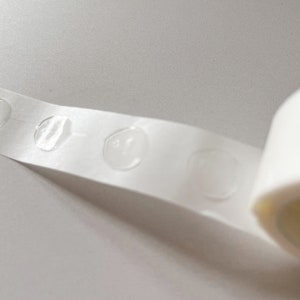 Detail of transparent glue dots roll unrolled. Each dot is double-sided and .47" round. 100 glue stickers per roll.