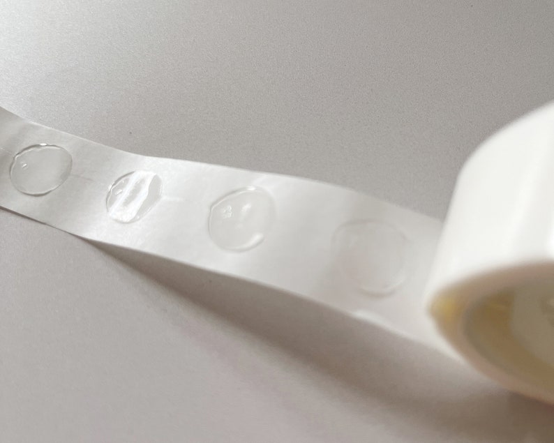 Detail of transparent glue dots roll unrolled. Each dot is double-sided and .47" round. 100 glue stickers per roll.