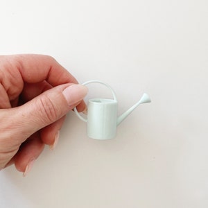 Miniature watering can in pale blue tone. Features round handle and long neck.