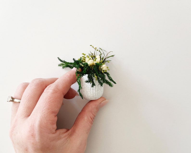 Miniature potted plant made from 100% natural preserved flowers and greenery. White flowers surrounded by green foliage in a stone textured pot.