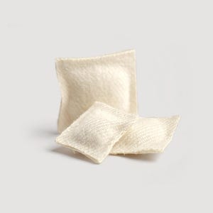 May include: Three small, off-white fabric items are arranged on a light background. One is a square shape, and two are rectangular. The fabric has a textured appearance, and the items appear to be soft.