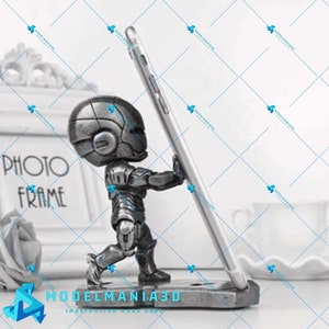 Könnte beinhalten: Eine silberne Roboterfigur, die ein Smartphone senkrecht hält. Der Roboter steht auf einem Sockel mit den Worten "MODELMANIA3D" und "IMAGINATION MADE REAL".