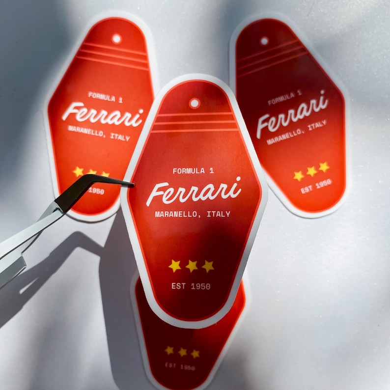 Może przedstawiać: Trzy czerwono-białe naklejki na breloki do motelu z napisem "Formuła 1 Ferrari Maranello, Włochy" i "Est 1950".