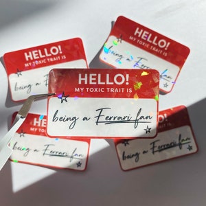 May include: Five red and white holographic stickers with the text "HELLO! MY TOXIC TRAIT IS being a Ferrari fan" on each. The stickers have a star on each side of the text.