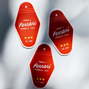 Może przedstawiać: Trzy czerwone naklejki w kształcie klucza z białym tekstem i ż&oacute;łtymi gwiazdami. Tekst brzmi "Formuła 1 Ferrari Maranello, Włochy Est 1950".