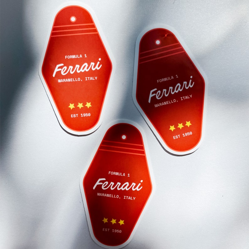 Może przedstawiać: Trzy czerwone naklejki w kształcie klucza z białym tekstem i ż&oacute;łtymi gwiazdami. Tekst brzmi "Formuła 1 Ferrari Maranello, Włochy Est 1950".