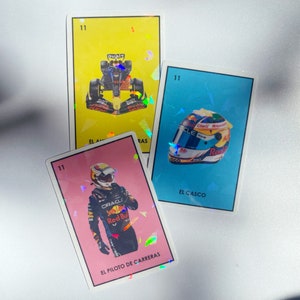 May include: Three colorful cards with a holographic finish. The cards feature images of a race car driver, a race car, and a racing helmet. The cards are numbered 11 and have the text "EL PILOTO DE CARRERAS", "EL AUTO", and "EL CASCO" printed on them.