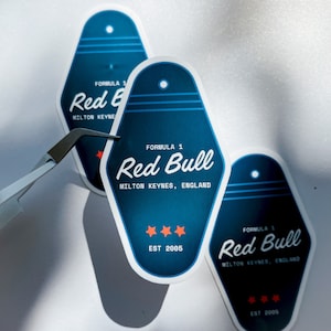 Könnte beinhalten: Drei blaue und weiße Motel-Schlüsselanhänger-Aufkleber mit dem aufgedruckten Text "Formel 1 Red Bull Milton Keynes, England Est 2005".