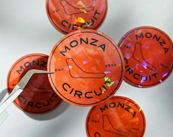 May include: Four orange and black circular stickers with a holographic finish. Each sticker features the text "MONZA CIRCUIT" and the year "1922" or "1923". The stickers also feature a stylized outline of a racetrack.