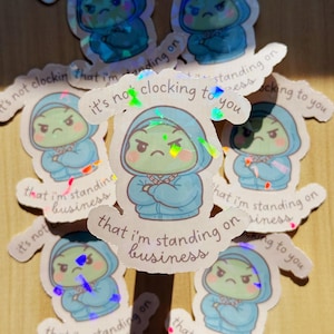 May include: A collection of holographic stickers featuring a cartoon character in a blue hoodie with arms crossed. The character has a green face and a stern expression. Text on the stickers reads "It's not clocking to you that I'm standing on business."