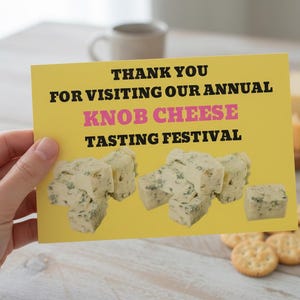 May include: A yellow card with the text "THANK YOU FOR VISITING OUR ANNUAL KNOB CHEESE TASTING FESTIVAL" is held in front of a light-coloured wooden surface. Cubes of cheese are pictured on the card. Crackers and a cheese wedge are also visible.