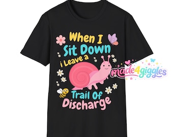Op de afbeelding: Een zwart t-shirt met korte mouwen met een roze slakafbeelding en de tekst "When I Sit Down i Leave a Trail Of Discharge". Het ontwerp bevat kleine bloemen, een bij en een vlinder, met de merknaam "made4giggles" in de hoek.