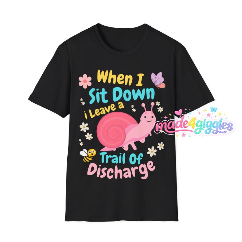 May include: A black short-sleeve t-shirt featuring a pink snail graphic and the text "When I Sit Down i Leave a Trail Of Discharge". The design includes small flowers, a bee, and a butterfly, with the brand name "made4giggles" in the corner.
