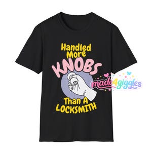 May include: Black t-shirt with the text "Handled More Knobs Than A Locksmith" in yellow and pink. The graphic shows a hand holding a doorknob inside a purple circle. The brand logo "made 4 giggles" is in the lower right corner.