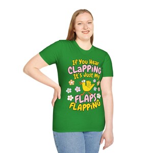 Może przedstawiać: Zielona koszulka z napisem "If You Hear CLAPPING It's Just My FLAPS FLAPPING". Koszulka przedstawia kresk&oacute;wkowego ż&oacute;łtego ptaka z pomarańczowymi nogami i dziobem, otoczonego kolorowymi kwiatami. Koszulka jest noszona przez osobę.