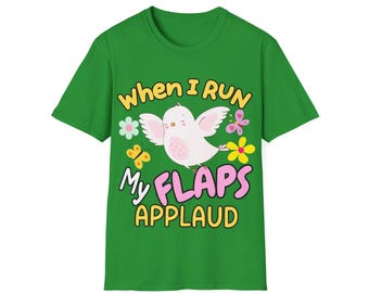 May include: A green short-sleeve t-shirt featuring a graphic of a white bird with pink wings. The text reads "WHEN I RUN MY FLAPS APPLAUD" in yellow and pink letters. The design includes small colorful flowers and butterflies surrounding the bird.