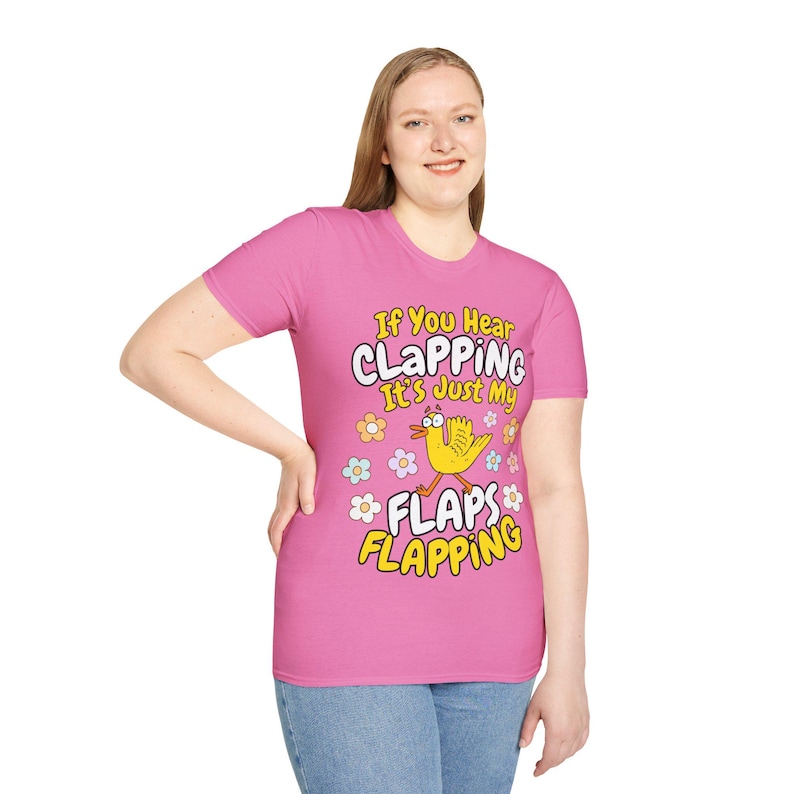 Może przedstawiać: R&oacute;żowa koszulka z napisem "If You Hear CLAPPING It's Just My FLAPS FLAPPING". Koszulka przedstawia ż&oacute;łtego ptaka z kresk&oacute;wek z pomarańczowymi stopami i dziobem, otoczonego kolorowymi kwiatami.