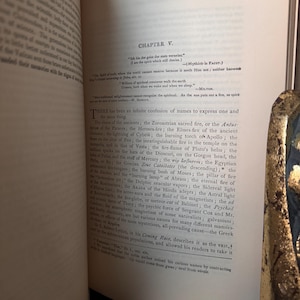 May include: An open book with text on aged paper. The text is in English and includes the chapter title "CHAPTER V." and a quote in German. The page has a decorative gold edge.