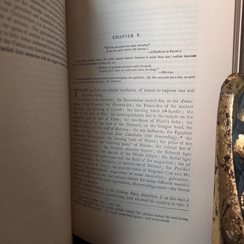 May include: An open book with text on aged paper. The text is in English and includes the chapter title "CHAPTER V." and a quote in German. The page has a decorative gold edge.