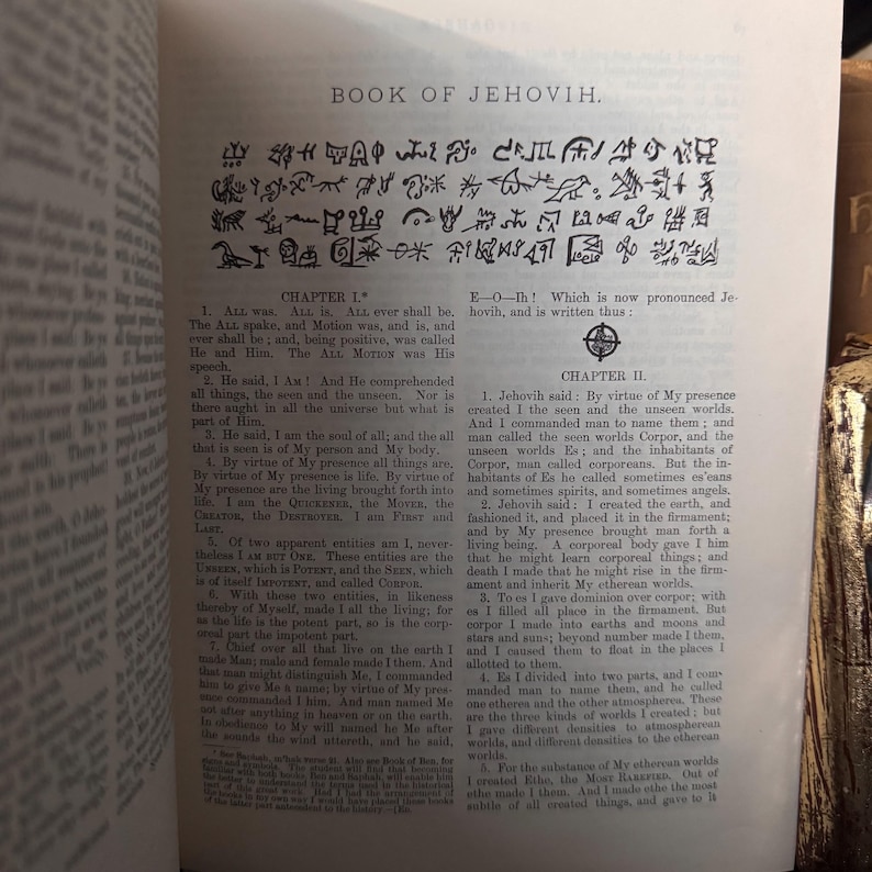 Pu&ograve; includere: Libro aperto con testo e simboli. Il titolo "BOOK OF JEHOVIH" &egrave; visibile in alto. Il testo &egrave; in inglese, con i titoli dei capitoli I e II. Le pagine sono ingiallite e invecchiate.