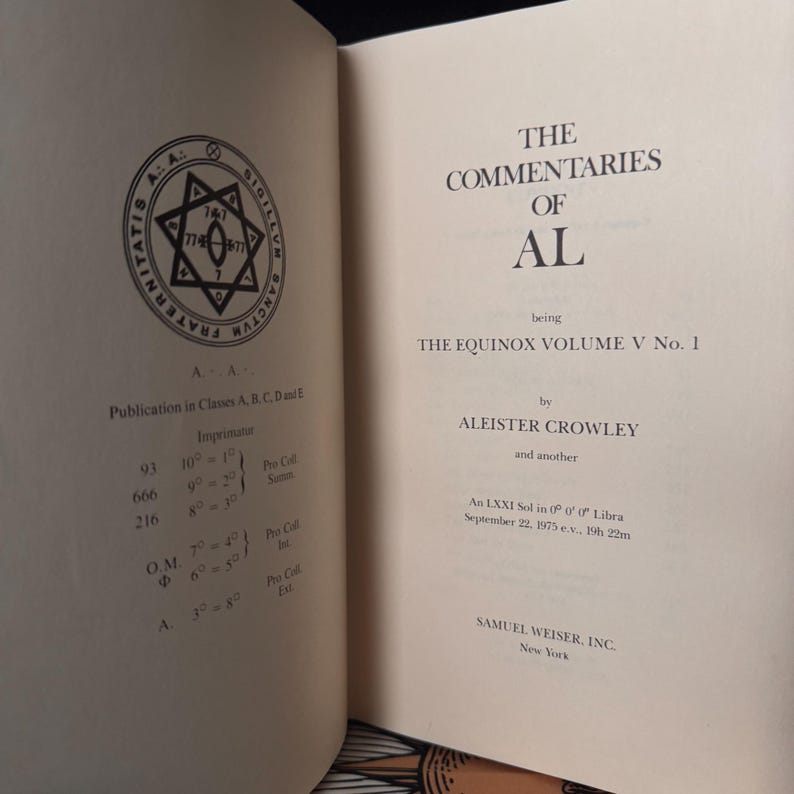 May include: Open book with the title "The Commentaries of AL" by Aleister Crowley. The book's pages are off-white, with text in black. A circular emblem with a star and text is on the left page. The book is part of "The Equinox Volume V No. 1".