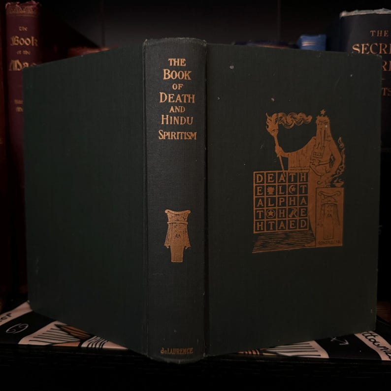 May include: A dark green hardcover book titled "The Book of Death and Hindu Spiritism" with gold lettering. The cover features a gold illustration of a figure holding a torch and a grid with the word "DEATH" spelled out.