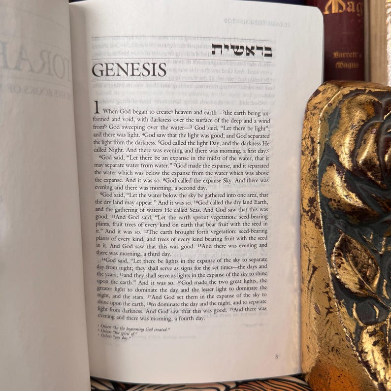 May include: Open Bible with the title "GENESIS" in English and Hebrew. The text describes the creation of the world. A decorative gold-colored object is partially visible on the right side of the image.