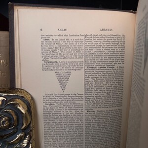 Puede incluir: P&aacute;gina de libro abierto con texto sobre "ABRAC" y "ABRAXAS". El texto est&aacute; en una fuente serif y la p&aacute;gina est&aacute; ligeramente amarillenta. El libro tiene un borde oscuro.