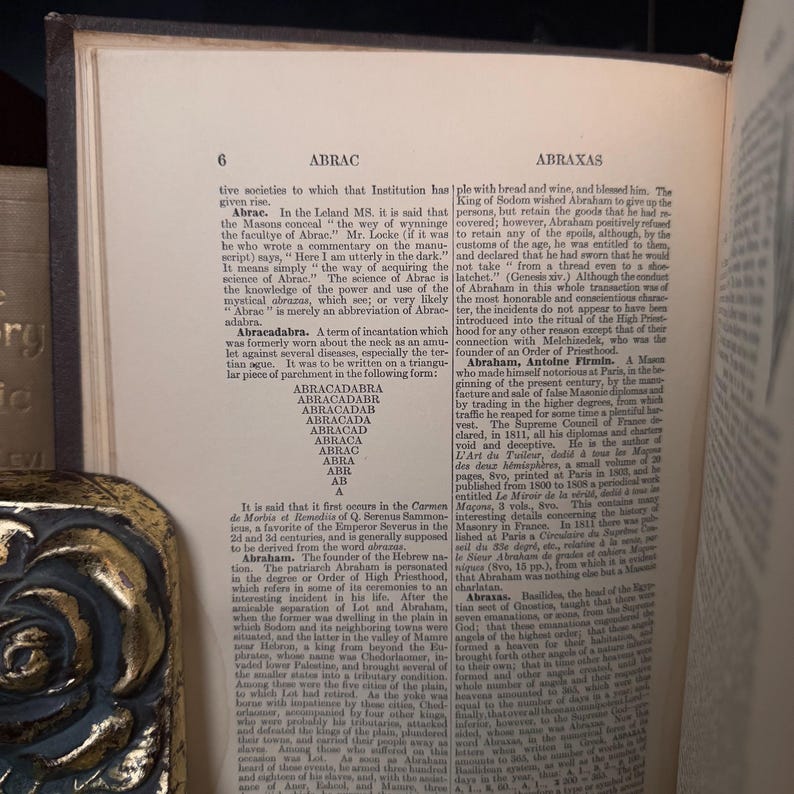 Puede incluir: P&aacute;gina de libro abierto con texto sobre "ABRAC" y "ABRAXAS". El texto est&aacute; en una fuente serif y la p&aacute;gina est&aacute; ligeramente amarillenta. El libro tiene un borde oscuro.