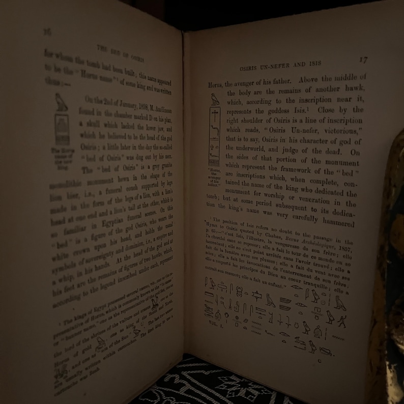 May include: A page from a book about the Egyptian god Osiris. The page features a black and white illustration of a hieroglyphic inscription and text that reads "Osiris Un-nefer and 1515". The text describes the god Osiris as the "avenger of his father" and the "judge of the dead".