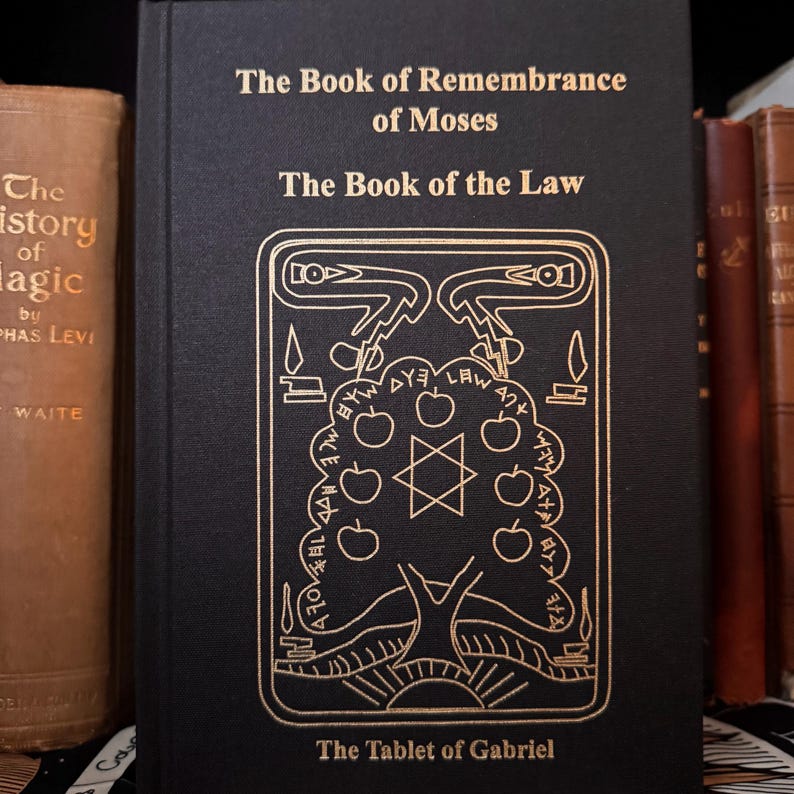 Peut inclure: Un livre noir avec des lettres dor&eacute;es, intitul&eacute; "The Book of Remembrance of Moses" et "The Book of the Law". La couverture pr&eacute;sente une illustration dor&eacute;e d'un arbre avec une &eacute;toile de David et d'autres symboles. Le texte "The Tablet of Gabriel" est en bas.