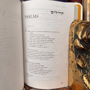 May include: Open book with the word "PSALMS" at the top of the page. The text is in English and Hebrew. A decorative gold-colored object is visible on the right side of the book.