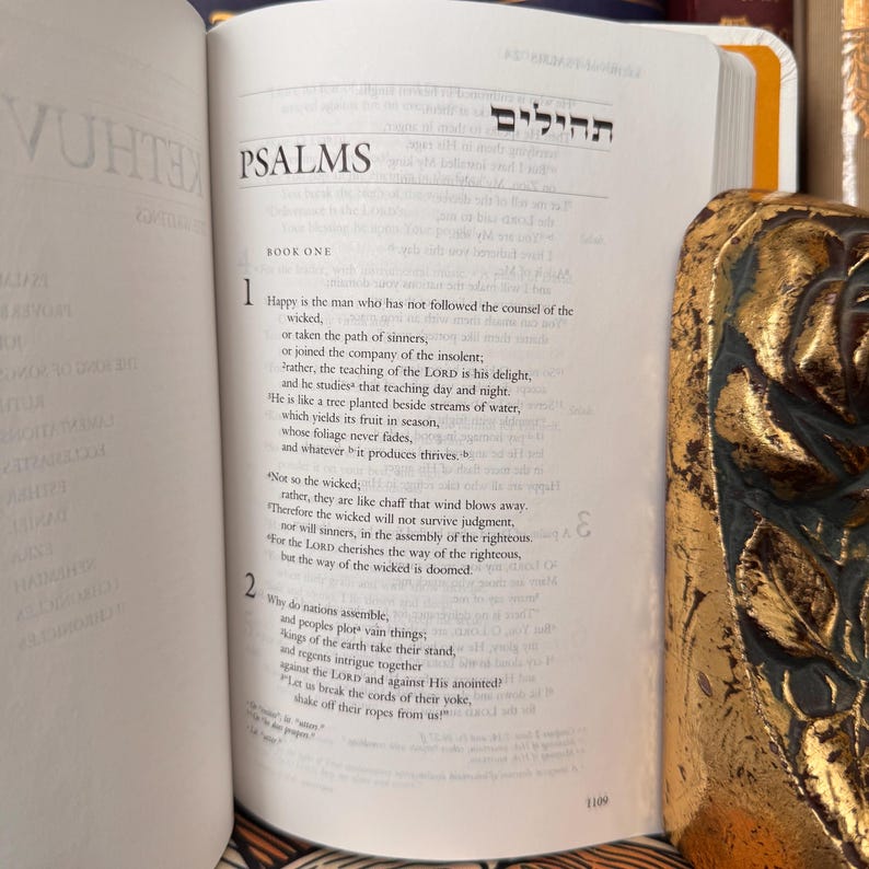 May include: Open book with the word "PSALMS" at the top of the page. The text is in English and Hebrew. A decorative gold-colored object is visible on the right side of the book.
