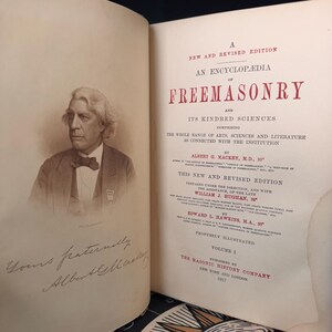 Puede incluir: Libro abierto con un retrato en sepia de un hombre con traje y pajarita. El t&iacute;tulo del libro es "An Encyclop&aelig;dia of Freemasonry". El libro es el Volumen 1, publicado en 1917 por The Masonic History Company.