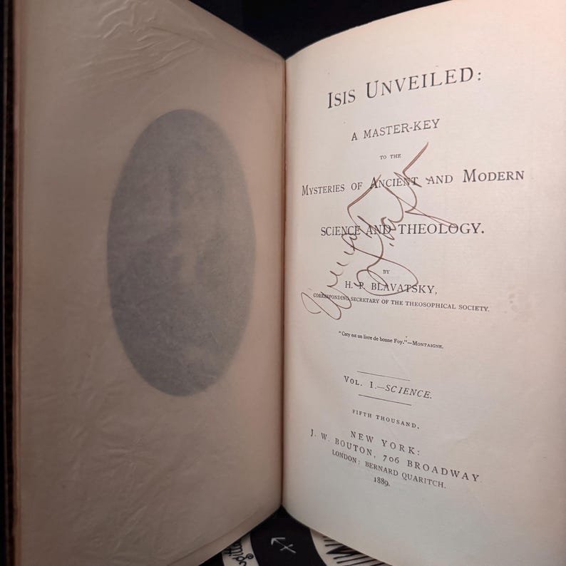 May include: Open book titled "Isis Unveiled: A Master-Key to the Mysteries of Ancient and Modern Science and Theology" by H.P. Blavatsky. The book is open to the title page, with a signature and the publisher's information.