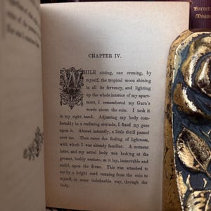 May include: A page from a book with the chapter title "Chapter IV." The text describes a person sitting in a room lit by moonlight, holding a coin. The text mentions a "Guru" and a "coin".