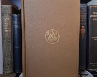 May include: A collection of antique books on a shelf. The central book is a light brown color with a gold emblem and the letters "TRY". Other books are visible in the background, with various colors and titles.