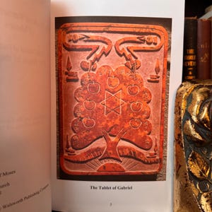 Peut inclure: Page d'un livre avec une illustration rouge-orang&eacute; d'une tablette. La tablette repr&eacute;sente un arbre avec des pommes, une &eacute;toile et du texte. Le texte en bas lit "The Tablet of Gabriel".