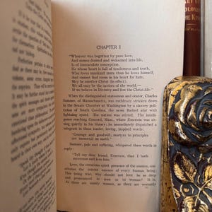 May include: An open book with a yellowed page, featuring a chapter titled "Chapter 1" and a passage about love and the Christ-life. The text is printed in black ink on a white background. The book is open to a page with a bookmark.