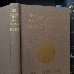 May include: The Sixth & Seventh Books of Moses on Magic Spirits. Art. A brown book with gold lettering and a gold circle with a design inside.