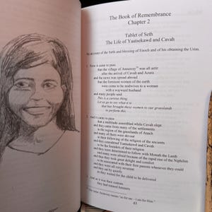 May include: An open book with text and a pencil sketch of a woman's face. The text is titled "The Book of Remembrance, Chapter 2" and details the "Tablet of Seth" and "The Life of Yaatsekawd and Cavah."
