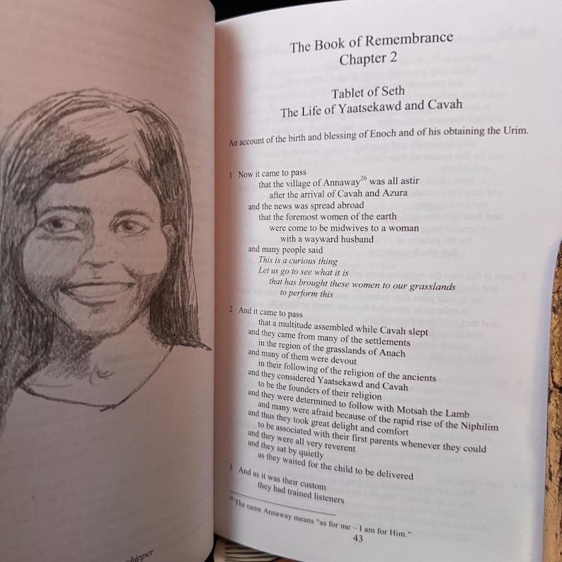 May include: An open book with text and a pencil sketch of a woman's face. The text is titled "The Book of Remembrance, Chapter 2" and details the "Tablet of Seth" and "The Life of Yaatsekawd and Cavah."