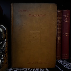 Könnte beinhalten: Ein altes Buch mit dem Titel "Dämonenbesessenheit" von Rev. John L. Nevius, D.D. Der Buchumschlag ist dunkelbraun mit goldenen Buchstaben und einem goldenen Prägedesign.