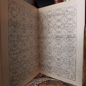 Op de afbeelding: Open boekpagina's met talrijke zwart-wit cirkelvormige illustraties. Elke cirkel bevat ingewikkelde, gestileerde symbolen en ontwerpen. De pagina's zijn verouderd, met een zichtbare vouw.