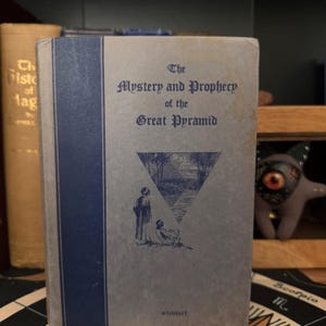 May include: A vintage book titled "The Mystery and Prophecy of the Great Pyramid" by Knight. The cover features a blue triangle with a drawing of a pyramid and two figures looking at it.