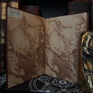 May include: An open book with marbled endpapers. The book is bound in red leather and has a label on the front cover that reads "W.M. Schaffer, Piano, Organ, and Church Music, Publisher, 401 Main Street,  Telephone 1111."
